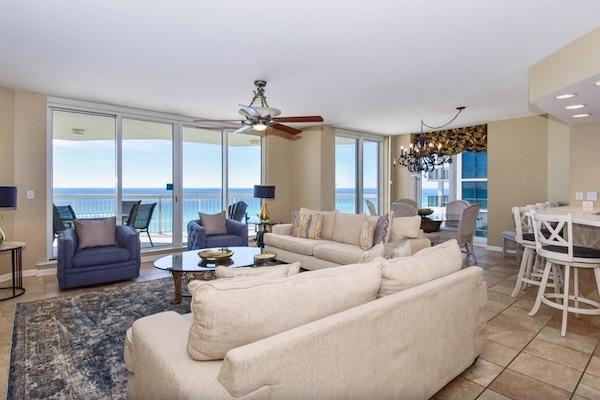 Living and dining area in a Silver Beach Towers 4 bedroom beachfront condo, with cream sofas, blue armchairs, and Gulf views through balcony doors.